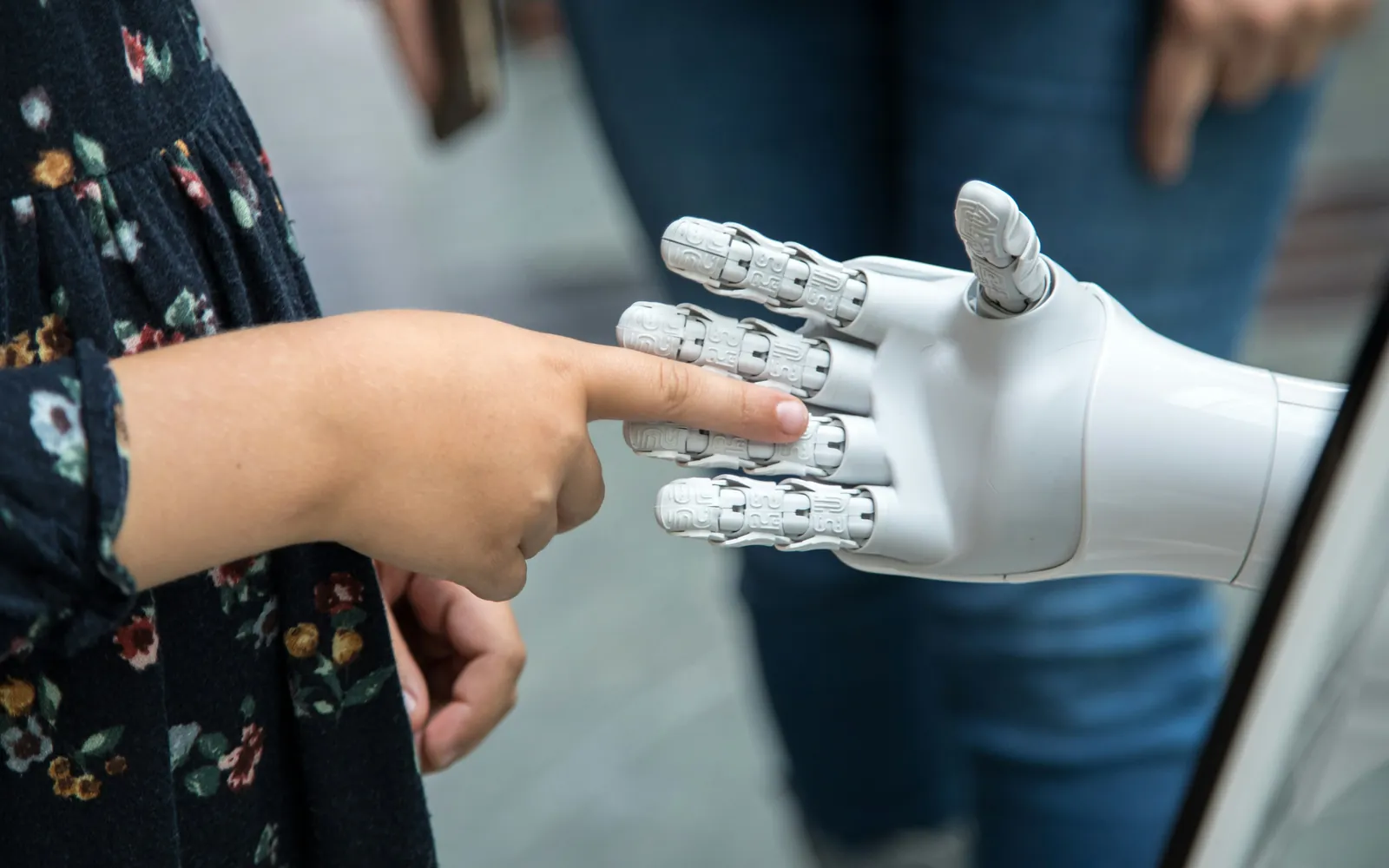Ein ausgestreckter Zeigefinger berührt die Fingerspitzen einer weißen Roboterhand