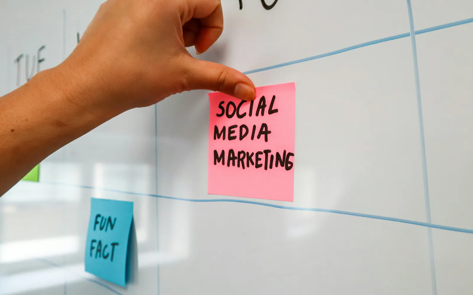 Eine Hand heftet einen pinken Notizzettel mit der Aufschrift „Social Media Marketing“ an eine Wand